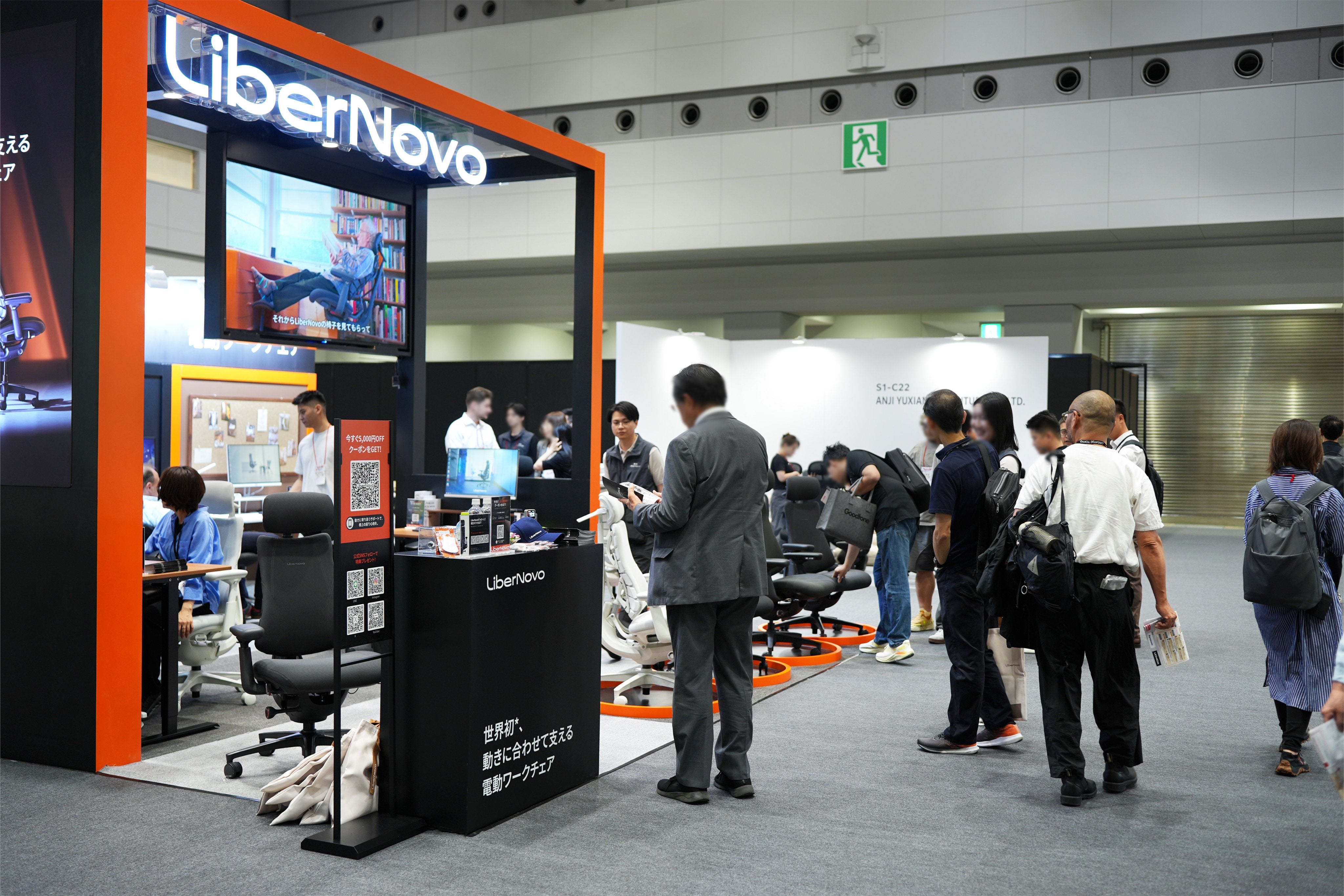 オルガテック東京2026の展示ブースにディスプレイされた高機能オフィスチェアと、賑わう会場の背景。